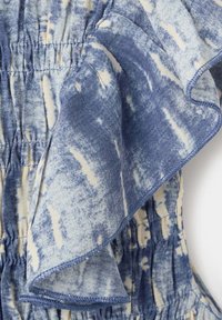 Tissu tie-dye bleu et blanc avec couture froncée et détail de bord à volants.