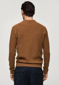 Brown ribbed knit sweater with a round neckline and long sleeves, featuring a fitted hem and neck. Worn with dark pants.
