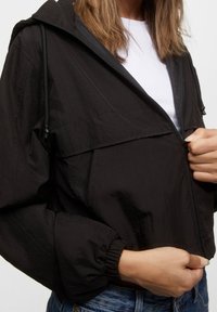 Czarna lekka kurtka z kapturem, elastycznymi mankietami i przednim zamkiem błyskawicznym. Gładka faktura, krótki fason i widoczne detale szwów.