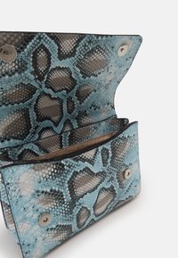 Borsa in pelle a stampa serpente blu e nera con una texture liscia, dotata di chiusura a pattina e hardware a scatto argentato. Sono visibili due scomparti interni.