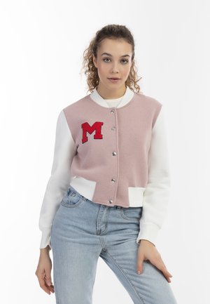 Roze en witte cropped varsityjack met zilveren drukknoopjes en een geborduurd rood "M" op de borst. Zacht materiaal met geribbelde manchetten.