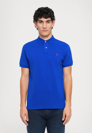 Blauwe polo met korte mouwen van gestructureerde stof, voorzien van een kraag met twee knopen en een rood logoaccent op de linkerborst.