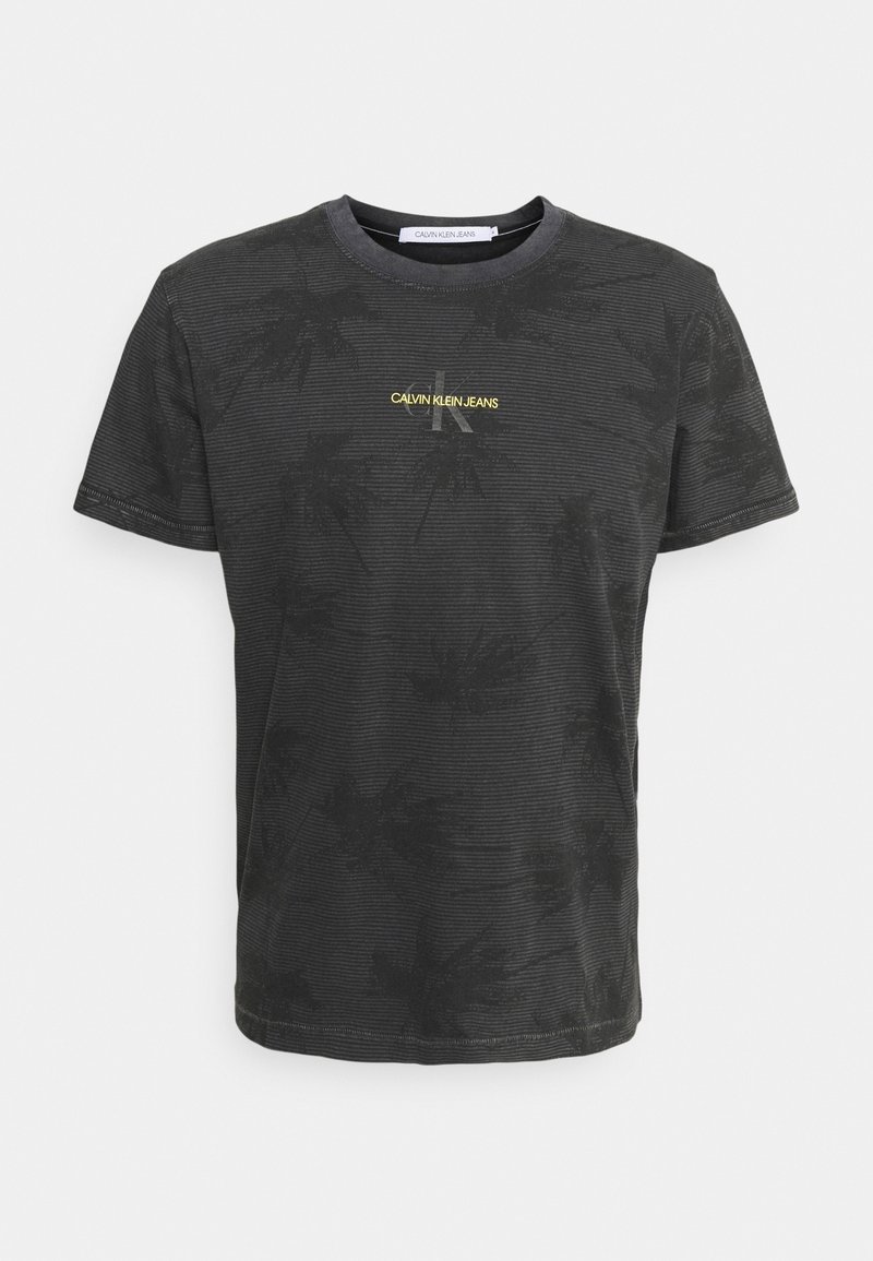 Black cotton t-shirt with a subtle palm leaf pattern, round neck, short sleeves, and yellow "CALVIN KLEIN JEANS" logo on the front.