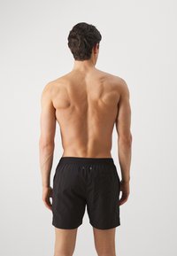 Costumi da bagno neri con vita elastica, due fori di aerazione e una tasca posteriore. Tessuto liscio e design lungo fino alla coscia.