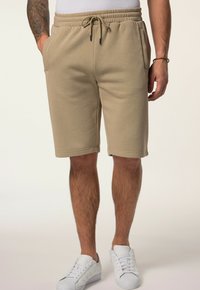 Beige cotton blend shorts with an elastic waistband, drawstring, and side pockets, ending just above the knee. Paired with white sneakers.