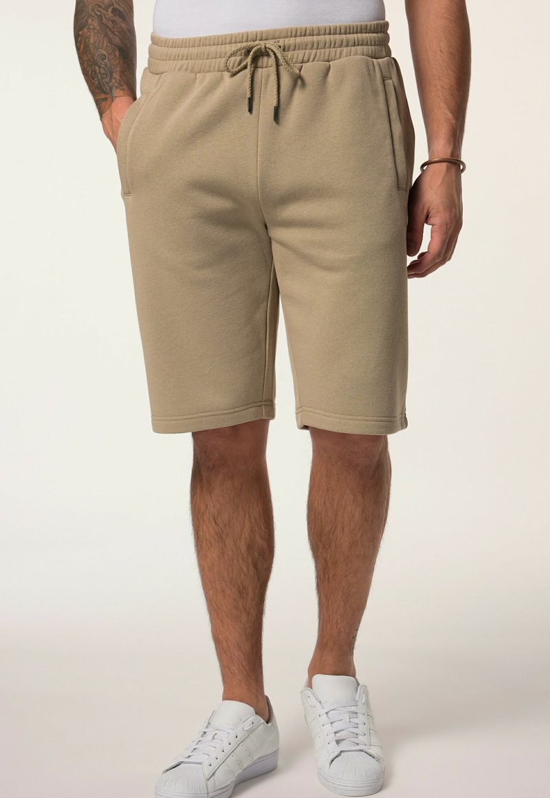 Beige cotton blend shorts with an elastic waistband, drawstring, and side pockets, ending just above the knee. Paired with white sneakers.