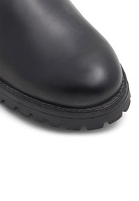 Bota de cuero negra con punta redondeada, parte superior texturizada y suela de goma gruesa con un diseño de dibujo para tracción.