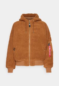 Hnědá fleecová bunda s kapucí, zipovým uzávěrem, žebrovanými manžetami a spodním lemem. Obsahuje zipovou kapsu s červeným štítkem. Texturovaný, teplý materiál.