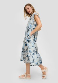 Blumenkleid in Hellblau und Grau mit kurzen �Ärmeln und Taschen. Kombiniert mit hellen geflochtenen Sandalen.