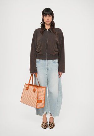 Καφέ φλις μπουφάν με φερμουάρ, ανοιχτό μπλε φθαρμένα παντελόνια με φαρδιά μπατζάκια, πορτοκαλί τσάντα ώμου με σχέδιο και loafers με λεοπάρ σχέδιο.