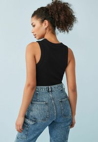 Sort ærmeløs tanktop med ribbet tekstur, parret med højtaljede blå denim cargo bukser med store baglommer.