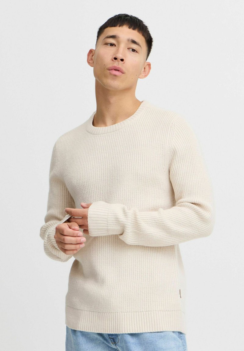 Beige ribbelgebreide trui met een ronde hals, lange mouwen en aangesloten manchetten. Lichtgewicht materiaal met een rechte zoom en subtiele textuur.