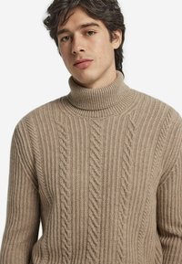 Beżowy sweter z torbą w sploty, z wysokim kołnierzem. Wykonany z miękkiego materiału, zaprojektowany z myślą o komforcie i cieple.