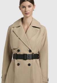 Beige doppelt geweven trenchcoat van soepel stof, met een grote kraag, zwarte riem en knopenaccenten.