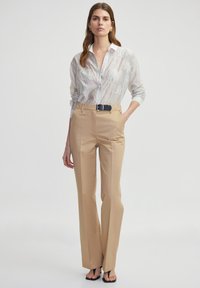 Camisa blanca de botones con rayas claras y patrones florales texturizados, combinada con pantalones de tiro alto en tono beige y zapatos de tacón abiertos negros.
