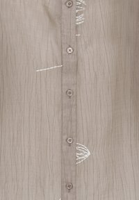 Chemise en tissu froissé beige avec des boutons verticaux et des accents brodés blancs subtils le long de la couture.