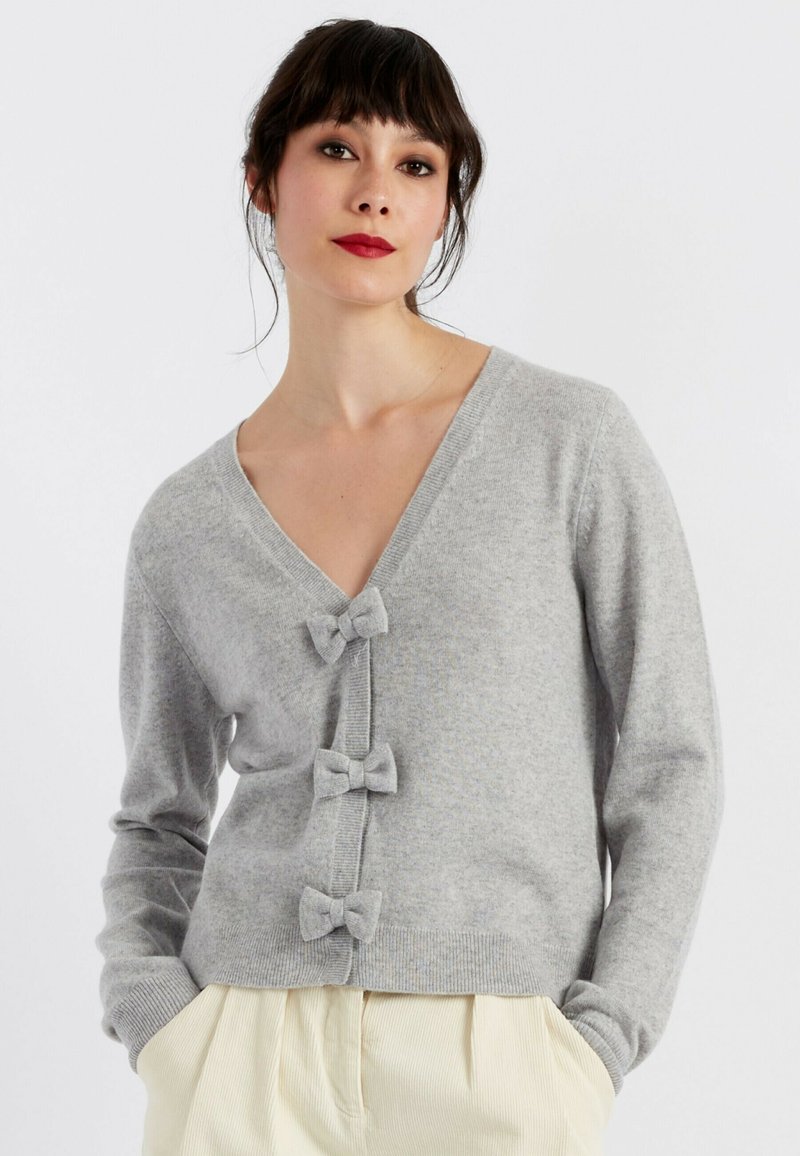 Cardigan grigio realizzato in morbido tessuto a maglia, con scollatura a V profonda, tre bottoni a forma di fiocco e orlo a costine per un finish testurizzato.