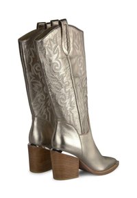 Srebrne metaliczne kowbojskie buty z ozdobnym haftem, średniej wysokości do łydki, kwadratowy nosek i masywne drewniane obcasy. Skórzane wykończenie o fakturowanej powierzchni.