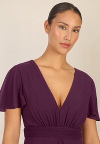 Vestido maxi de ciruela con un profundo escote en V, mangas cortas tipo volantes y detalle de cintura fruncida. La suave y fluida tela realza la silueta.