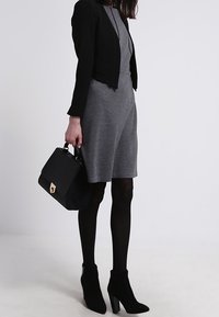 Grå klänning i mjukt tyg, kombinerad med en svart kort blazer. Accessoarer består av en svart handväska med struktur och svarta ankelboots med klack.