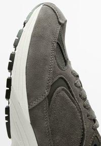 Baskets en suede gris avec une tige texturée, des accents en maille, des lacets ronds, et une semelle en caoutchouc blanche avec un motif de traction.