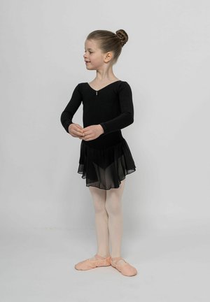 Schwarzer Langarm-Leotard mit tiefem Ausschnitt, geschichteter, transparenter schwarzer Rock und rosafarbene Ballettschuhe. Ballettpose vor neutralem Hintergrund.