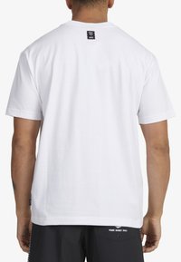 White short-sleeve T-shirt with a round neckline, smooth texture, and a black label on the back featuring text.