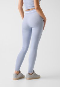 Hellblaue Leggings aus einem strukturierten Stoff, mit hohem Bund und enger Passform, kombiniert mit hellgrauen Turnschuhen.