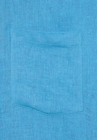 Μπλε λινό ύφασμα με υφή στην επιφάνειά του. Ένας παPatch τσέπης είναι ραμμένος πάνω στο κύριο ύφασμα, με ευθείες άκρες και ελάχιστη ραφή.