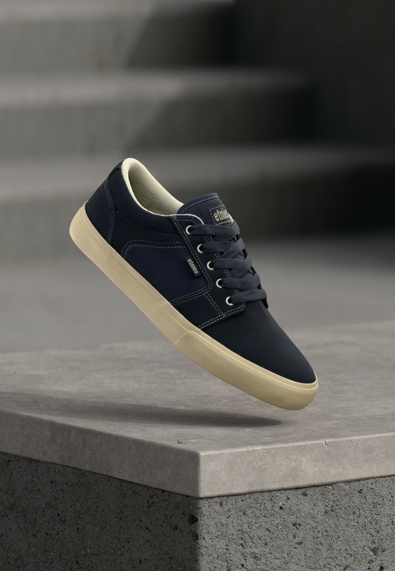 Sneaker en cuir navy avec semelle en caoutchouc crème, bout rond, design à lacets, avec des coutures tonalités et un petit patch logo sur la languette.