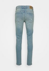 Light blue skinny jeans made of denim, featuring a textured finish, subtle distressing on the back pocket, and a branded brown leather tag.