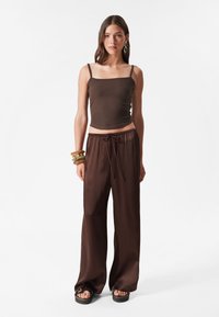 Brown cropped tank top with thin straps, paired with brown wide-leg pants featuring an elastic waistband and side drawstring. Sandals with thick soles.