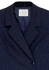 Temno modra teksturirana suknja z blazerjem s širokimi klapnicami, zapiranje na en črn gumb in viden oznako blagovne znamke NA-KD znotraj ovratnika.