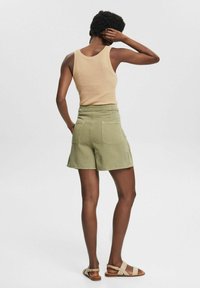 Beige ribbad toppi paritettu oliivinvihreiden sortsejen kanssa, joissa on takatasku. Shortseissa on rento istuvuus ja lahkeet ulottuvat puoliväliin reisiä.