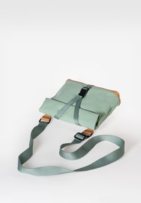 Borsa roll-top verde con dettagli in pelle marrone, tracolla regolabile e accessori neri. Texture liscia con un design minimalista.
