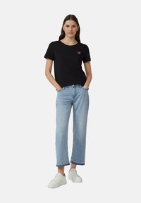 Zwarte katoen t-shirt met korte mouwen en ronde hals, voorzien van een klein rood accent ontwerp. Gepaard met lichtgewassen denim, verkort tot de enkels.