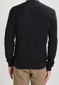 Black sweatshirt made of soft fleece, featuring a ribbed crew neck, long sleeves, and a fitted waistband. Textured surface with no patterns.