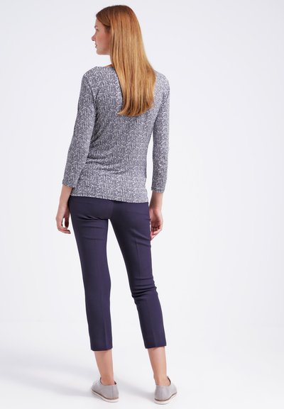 Haut à manches longues gris et blanc à motif, associé à un pantalon noir marine court et des chaussures slip-on gris clair. Tissu lisse, design ajusté.