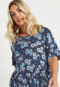 Marinblå blommig klänning med vita och blå blommönster, korta volangärmar och en utsvängd botten. Mjuktyg med en avslappnad passform.