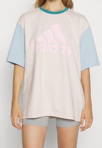 Adidas oversized t-shirt i ljusrosa med ljusblå korta ärmar, med en stor rosa logotyp på framsidan, av bomullsmaterial, avslappnad design.