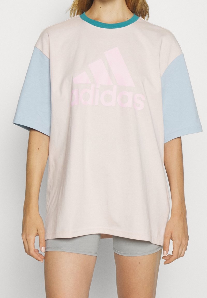 Adidas oversized t-shirt i ljusrosa med ljusblå korta ärmar, med en stor rosa logotyp på framsidan, av bomullsmaterial, avslappnad design.
