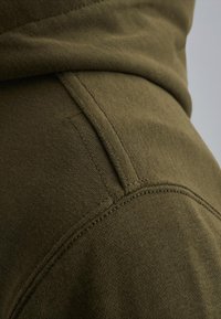 Primo piano di un tessuto verde oliva con cuciture dettagliate e linee di cucitura, che mette in evidenza la texture e la costruzione del capo.
