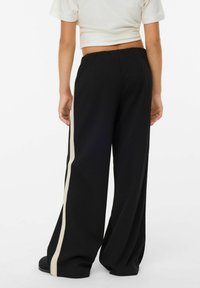 Svarta byxor med vida ben och en vit sidolinje, tillverkade av mjukt tyg, med elastisk midja och flytande fall för komfort.