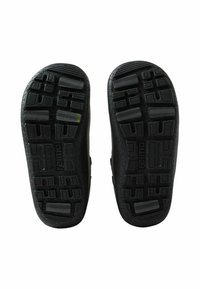 Czarne gumowe podeszwy butów z teksturowanymi wzorami, wyposażone w głębokie rowki zapewniające przyczepność. W centrum każdej podeszwy znajduje się logo marki.