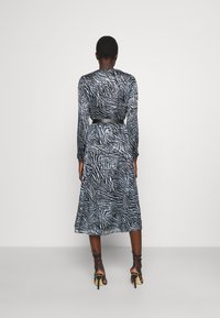 Svart och vit zebra-randig långärmad klänning med åtsittande midja, tillverkad av genomskinligt tyg, och matchad med strappy högklackade sandaler.