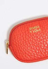 Bolso texturizado rojo con un zipper dorado y el logo en relieve "BIMBA Y LOLA" en la parte frontal. Presenta una forma redondeada y está hecho de material de cuero suave.