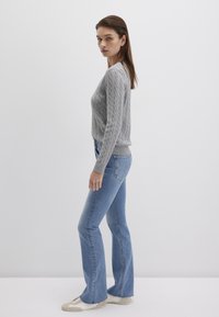 Grauer Strickpullover mit Rundhalsausschnitt, kombiniert mit hochtaillierten blauen Trompetenjeans und hellfarbigem Schuhwerk.