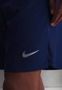 Person wearing dark blue Nike shorts with a reflective silver Nike swoosh logo near the hem.