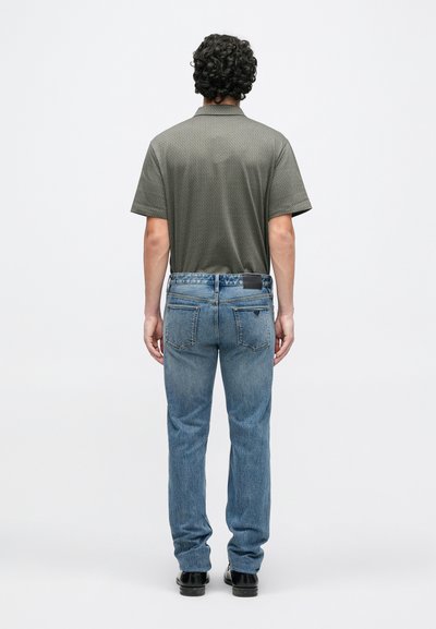 Γκρι πόλο με σχέδιο, σε συνδυασμό με μπλε τζιν παντελόνι. Τα εφαρμοστά τζιν έχουν δερμάτινο σημείο και κλασικές τσέπες. Μαύρα παπούτσια ολοκληρώνουν την εμφάνιση.