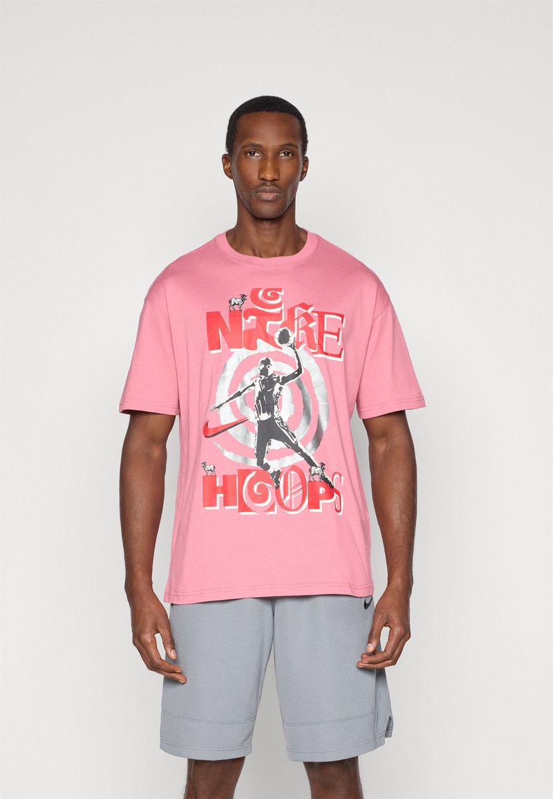 T-shirt di cotone rosa con stampa grafica di un giocatore di basket, con il testo "NIKE HOOPS" in colori rosso e nero in grassetto.